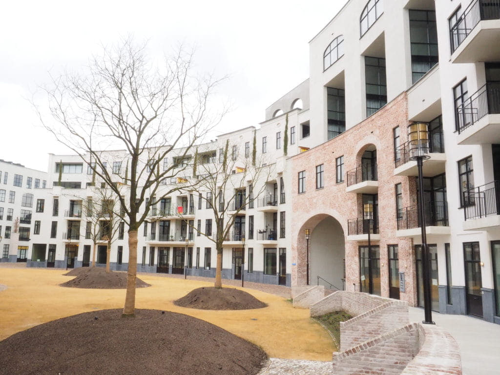 Binnenplaats met net geplante bomen en een ronde gevel met verschillende typen ramen en kleuren