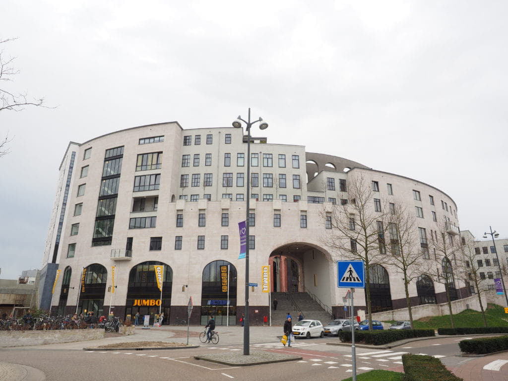 Buitenkant van het Maankwartier in Heerlen, een rond gebouw met bogen en een wittige gevel