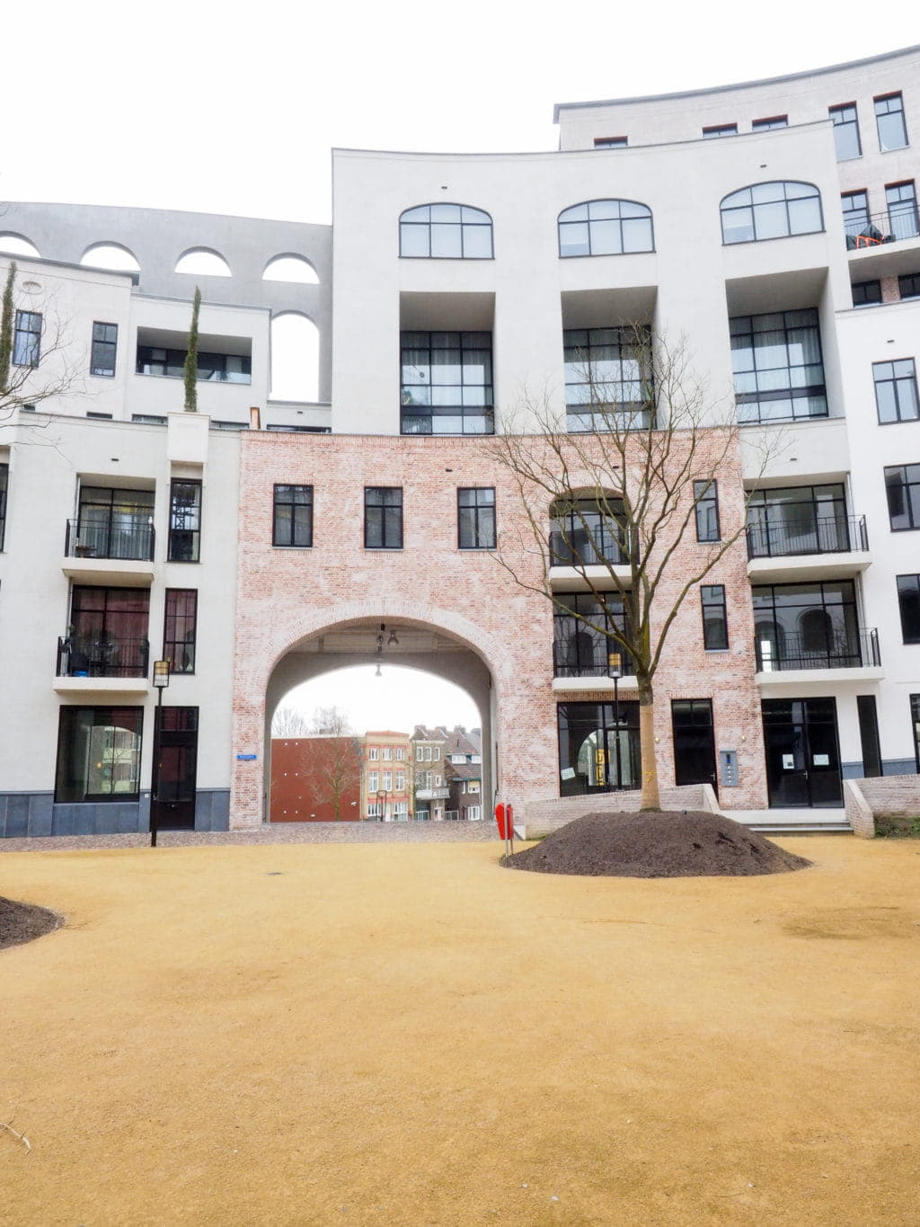 Binnenplaats met net geplante bomen en een ronde gevel met verschillende typen ramen en kleuren