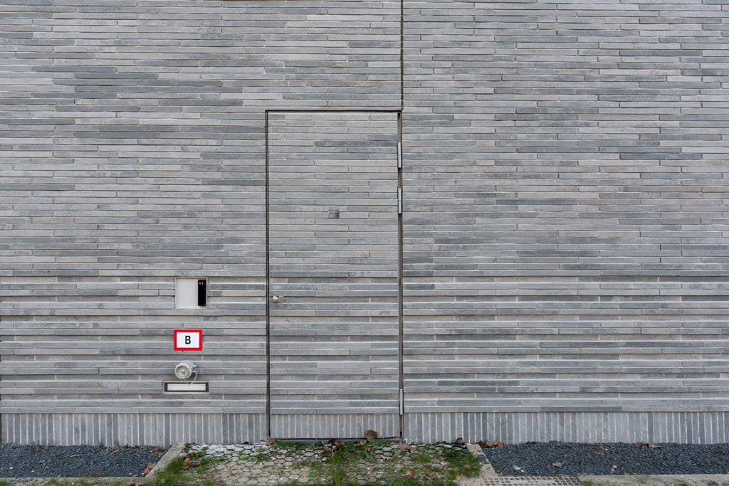 Detail van gevel met betonnen steenstrips langformaat, met een deur in de gevel