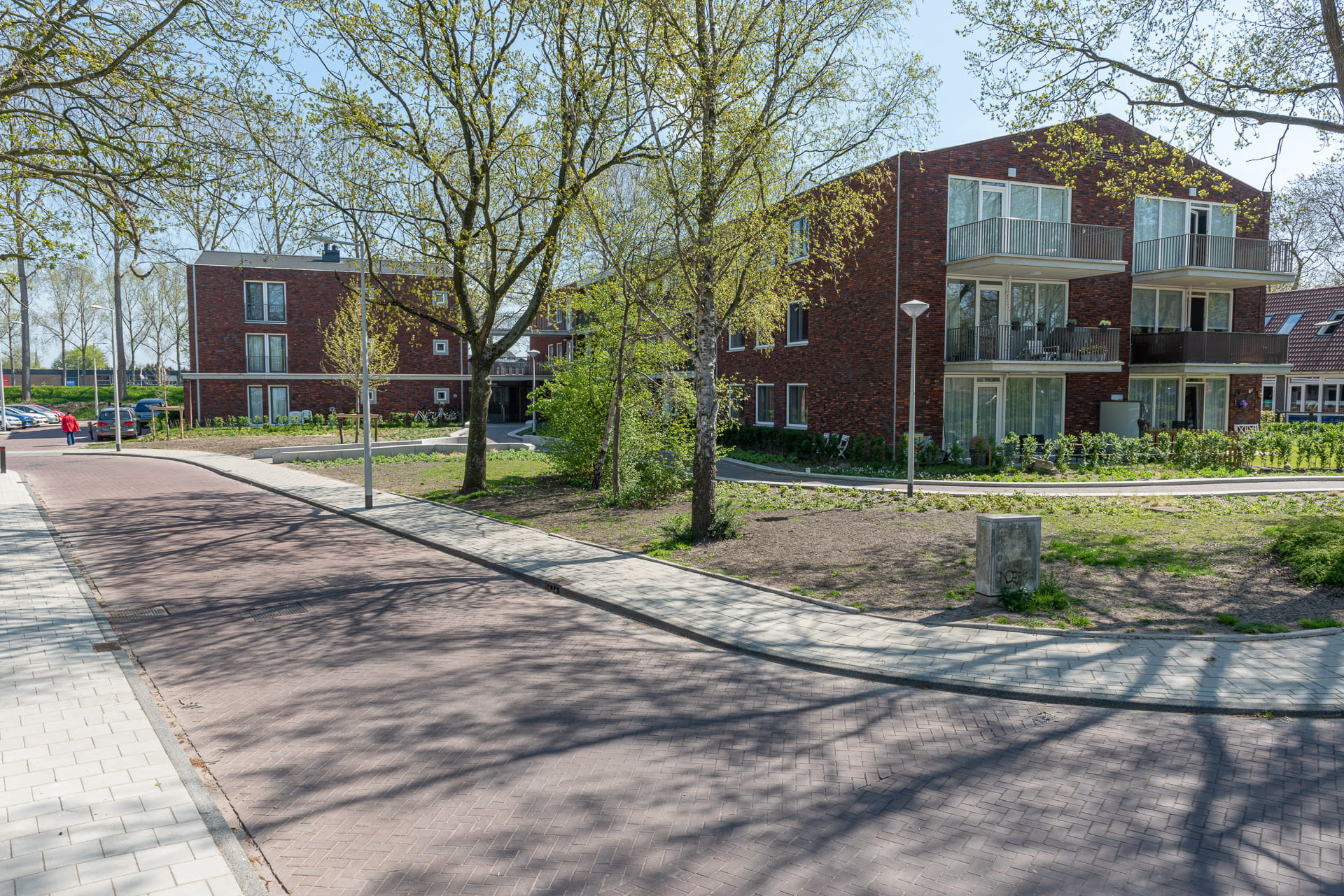 Vanaf een weg zicht op een roodbruin gebouw met bomen op de voorgrond