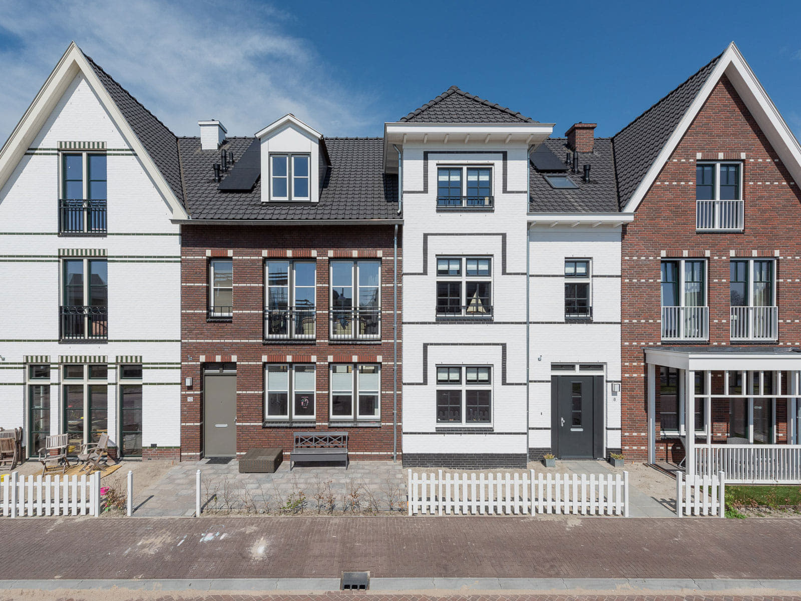 Rij van vier woningen in eind negentiende eeuwse stijl, maar nieuwgebouwd in verschillende kleuren wit en rood/bruin