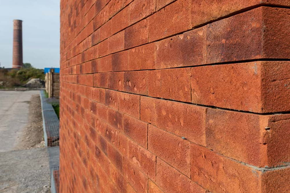 Rode muur met steenstrips met op de achtergrond een industrieterrein