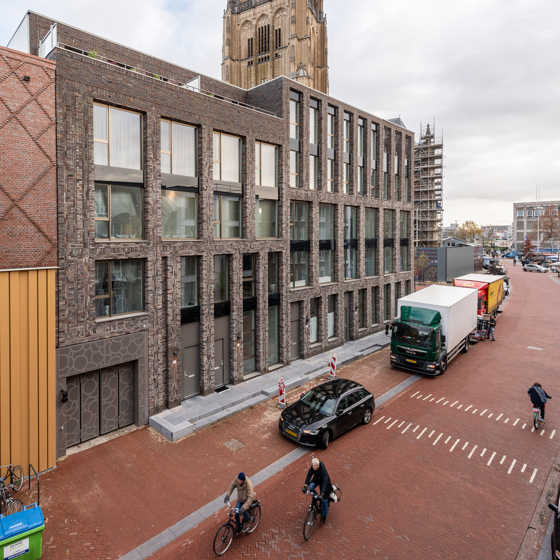 Gebouw met lichte gevel met op de voorgrond een straat met fietsers en auto's en busjes