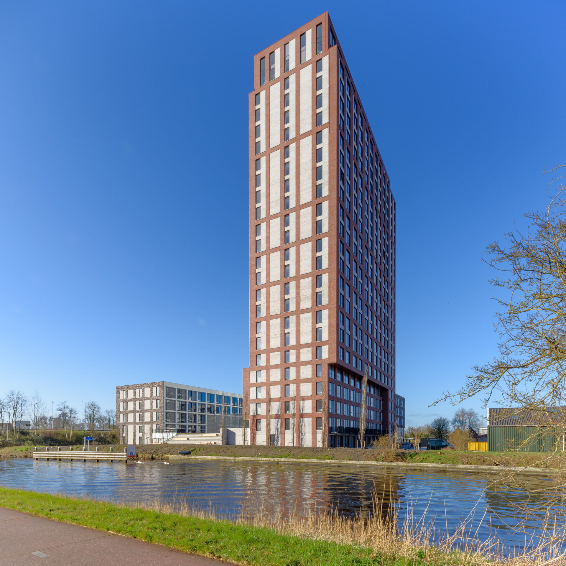 Een toren van rode en witte vlakken tegen een blauw lucht en op de voorgrond water