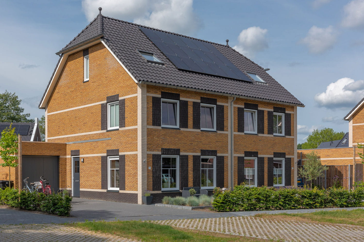 Twee-onder-een-kap met gelige bakstenen en een oprit ervoor, op het dak liggen donkere dagpannen en zonnepanelen
